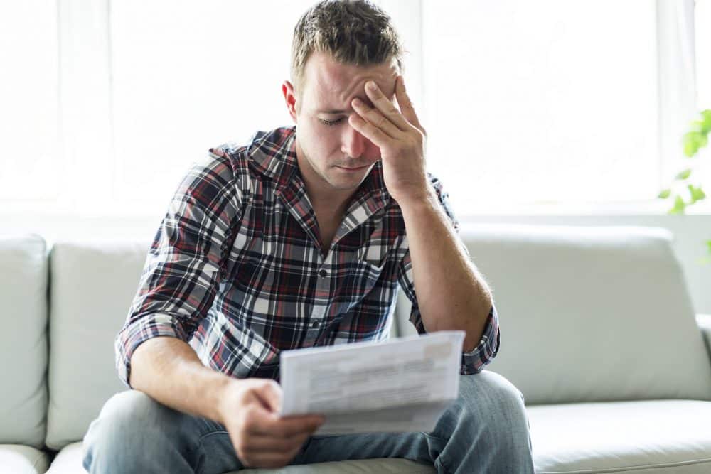 A man feeling stressed reading through his bills after a car accident in Midland, TX.