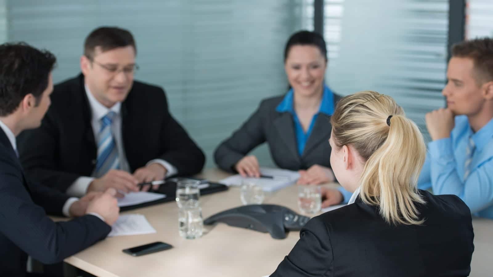 A group of business professionals in formal attire engaged in a discussion around a conference table.